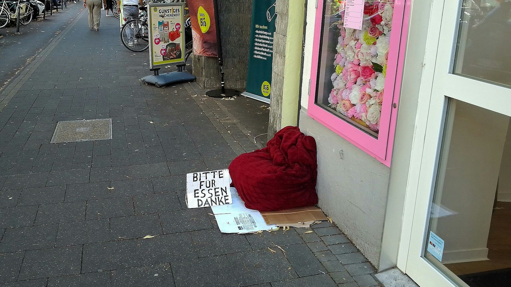 Neben einem Geschäftseingang liegt ein Kissen, daneben ein Schild mit der Aufschrift: „Bitte für Essen Danke“.