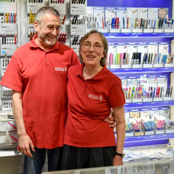 Eine Frau und ein Mann in roten Polohemden stehen vor einer Wand mit Stiften.
