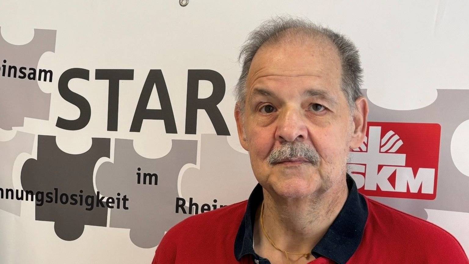Auf dem Bild ist das Portrait eines Mannes zu sehen, er trägt ein rotes Poloshirt.