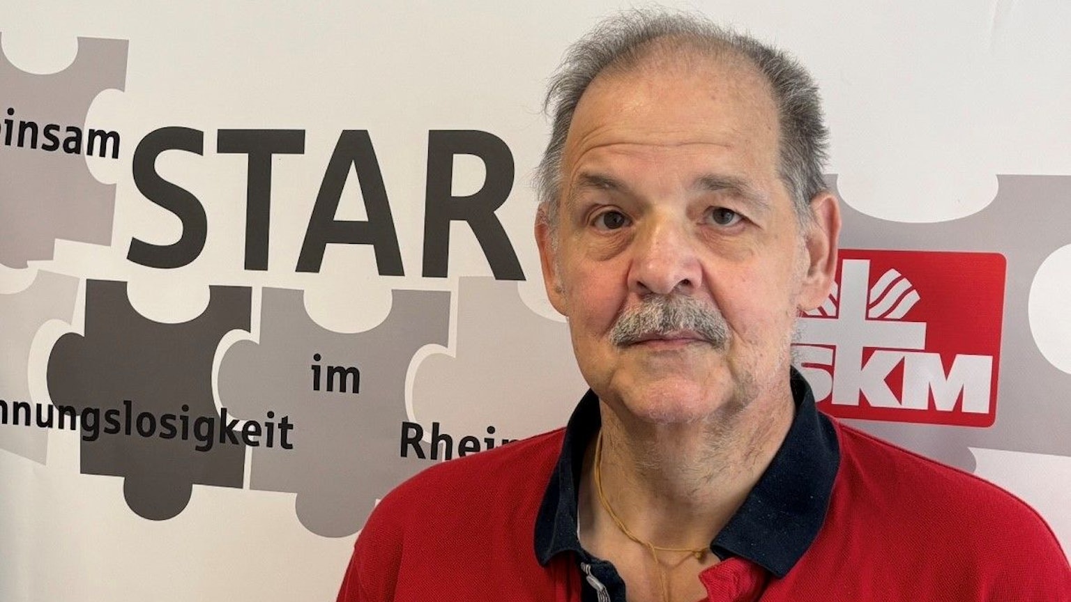 Auf dem Bild ist das Portrait eines Mannes zu sehen, er trägt ein rotes Poloshirt.