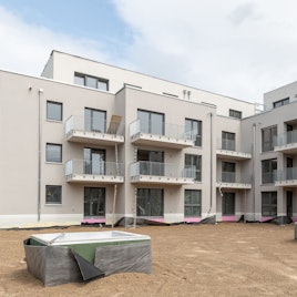 Das Bild zeigt eine der fertigen Wohnhäuser mit drei Geschossen und einem vierten Staffelgeschoss.