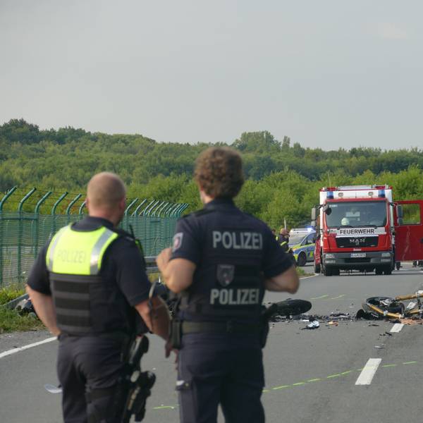 Polizisten blicken in Richtung der Unfallstelle auf der Alten Kölner Straße.