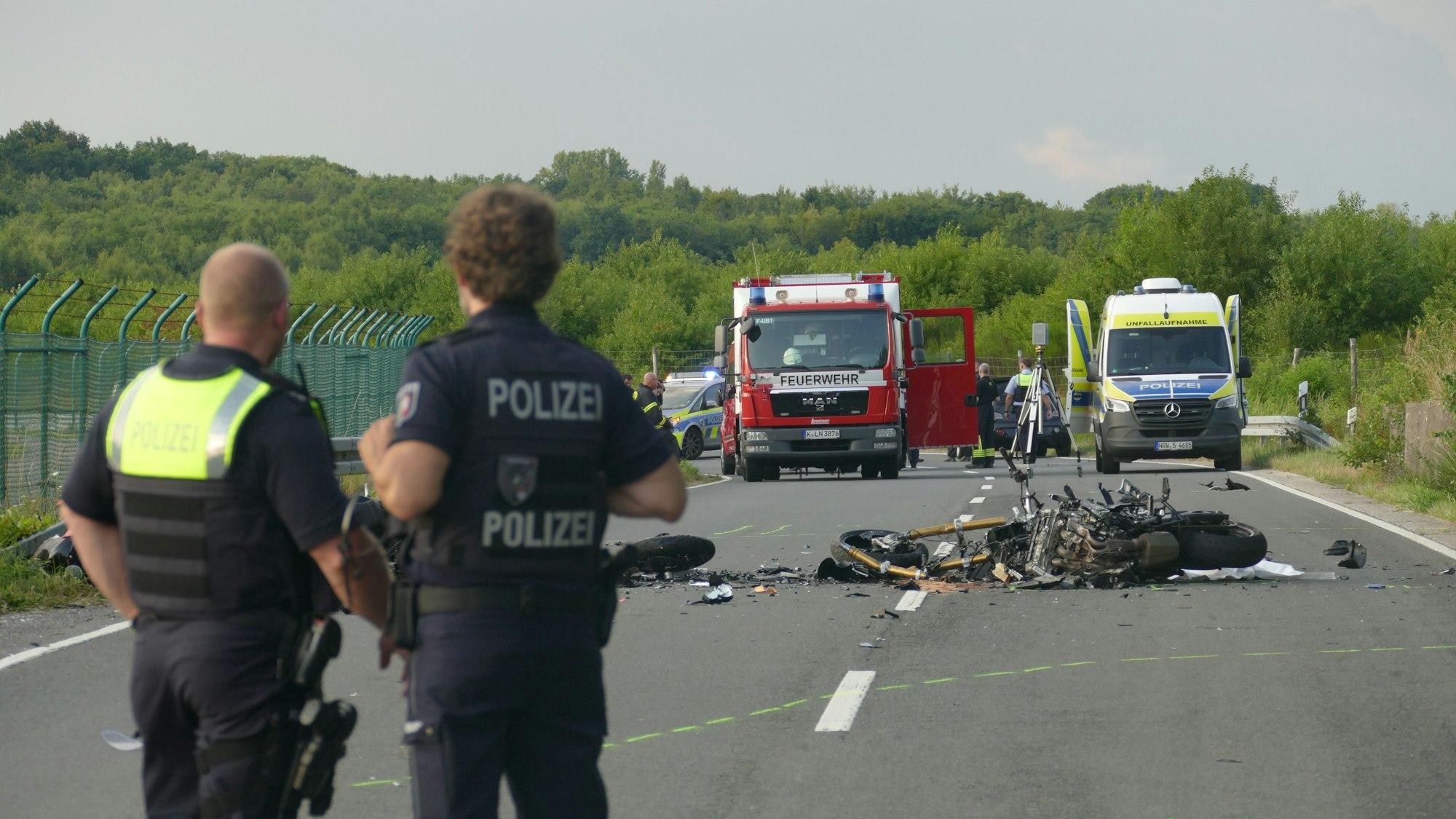 Polizisten blicken in Richtung der Unfallstelle auf der Alten Kölner Straße.