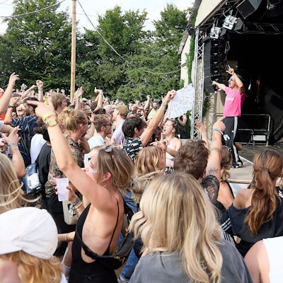 Der Rapper Dennis Dies Das steht mit erhobenen Armen auf der Bühne, davor steht eine große Menge Zuschauer und tanzt.