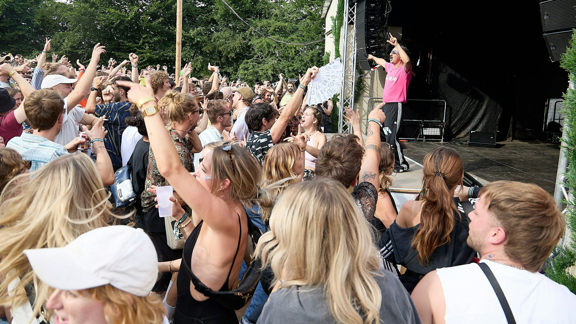 Der Rapper Dennis Dies Das steht mit erhobenen Armen auf der Bühne, davor steht eine große Menge Zuschauer und tanzt.