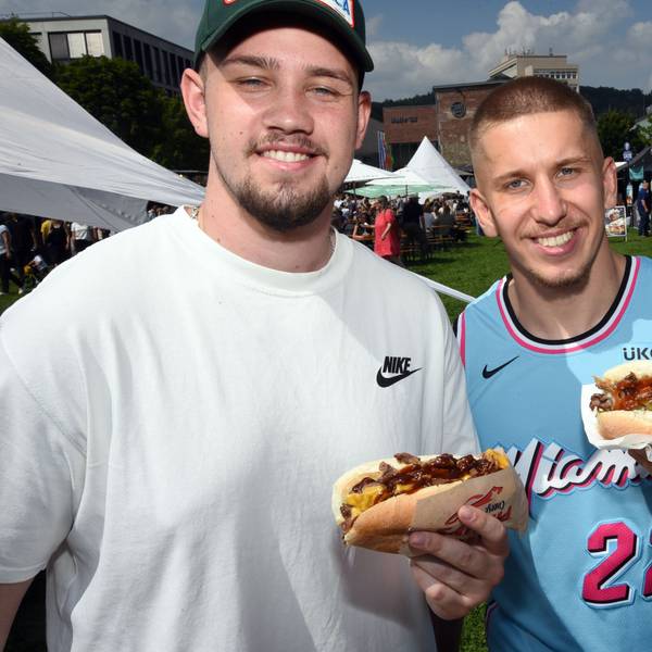 Zwei Männer halten ihr Essen grinsend in die Kamera.