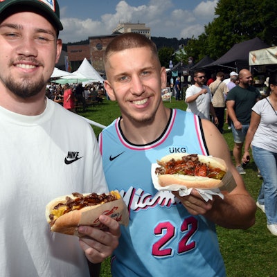 Zwei Männer halten ihr Essen grinsend in die Kamera.