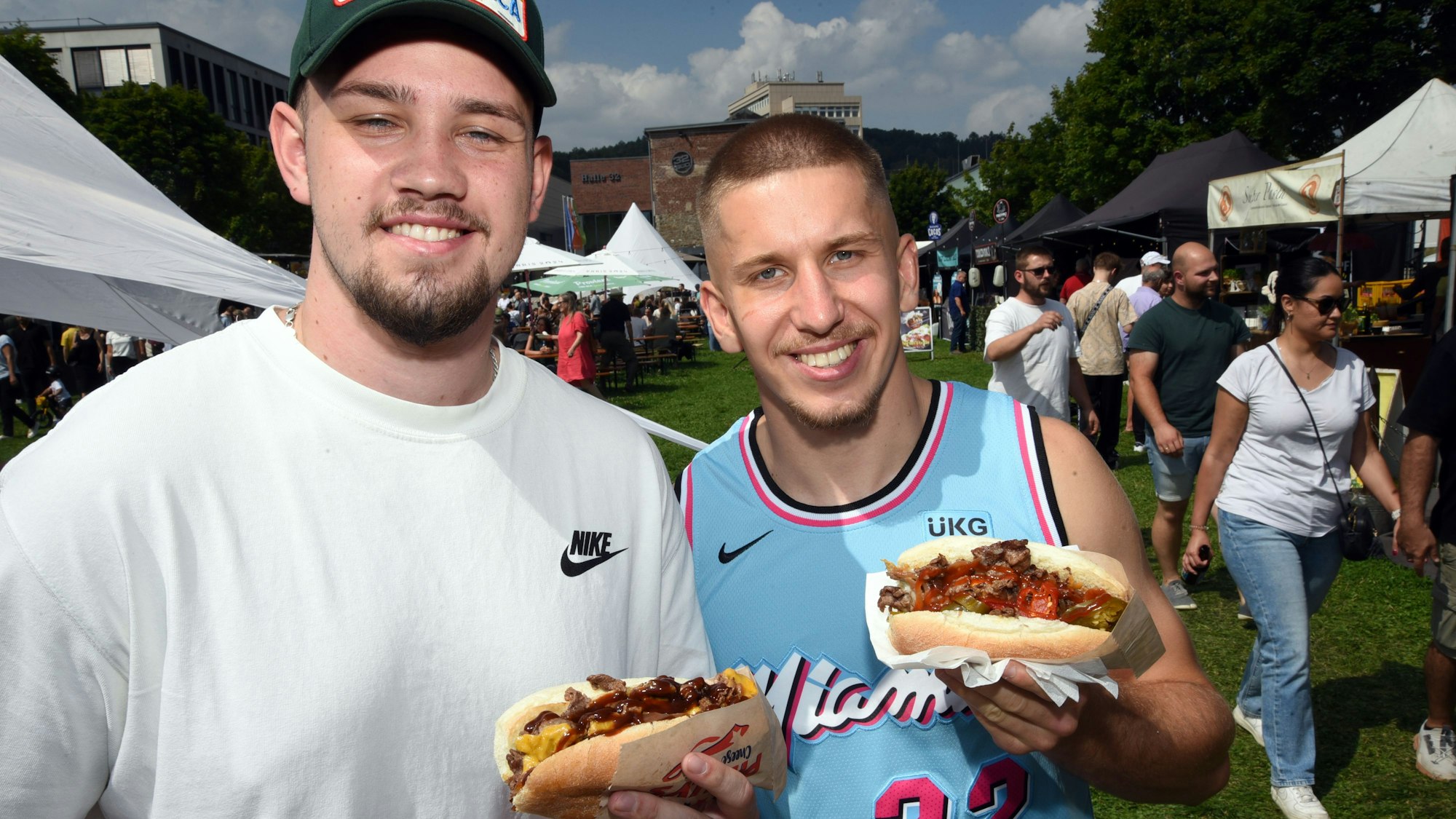 Zwei Männer halten ihr Essen grinsend in die Kamera.