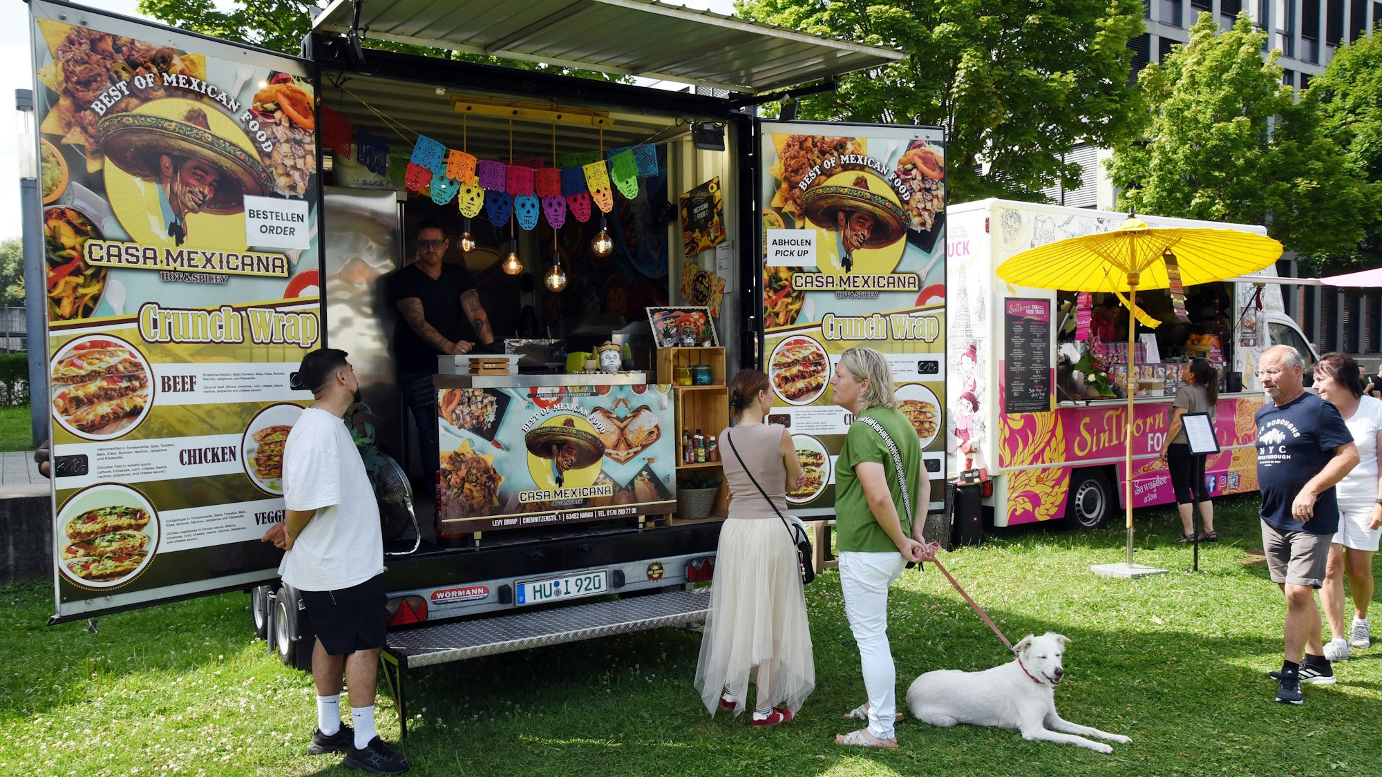 Ein paar Leute mit einem weißen Hund stehen vor dem mexikanischen Foodtruck "Casa Mexicana".