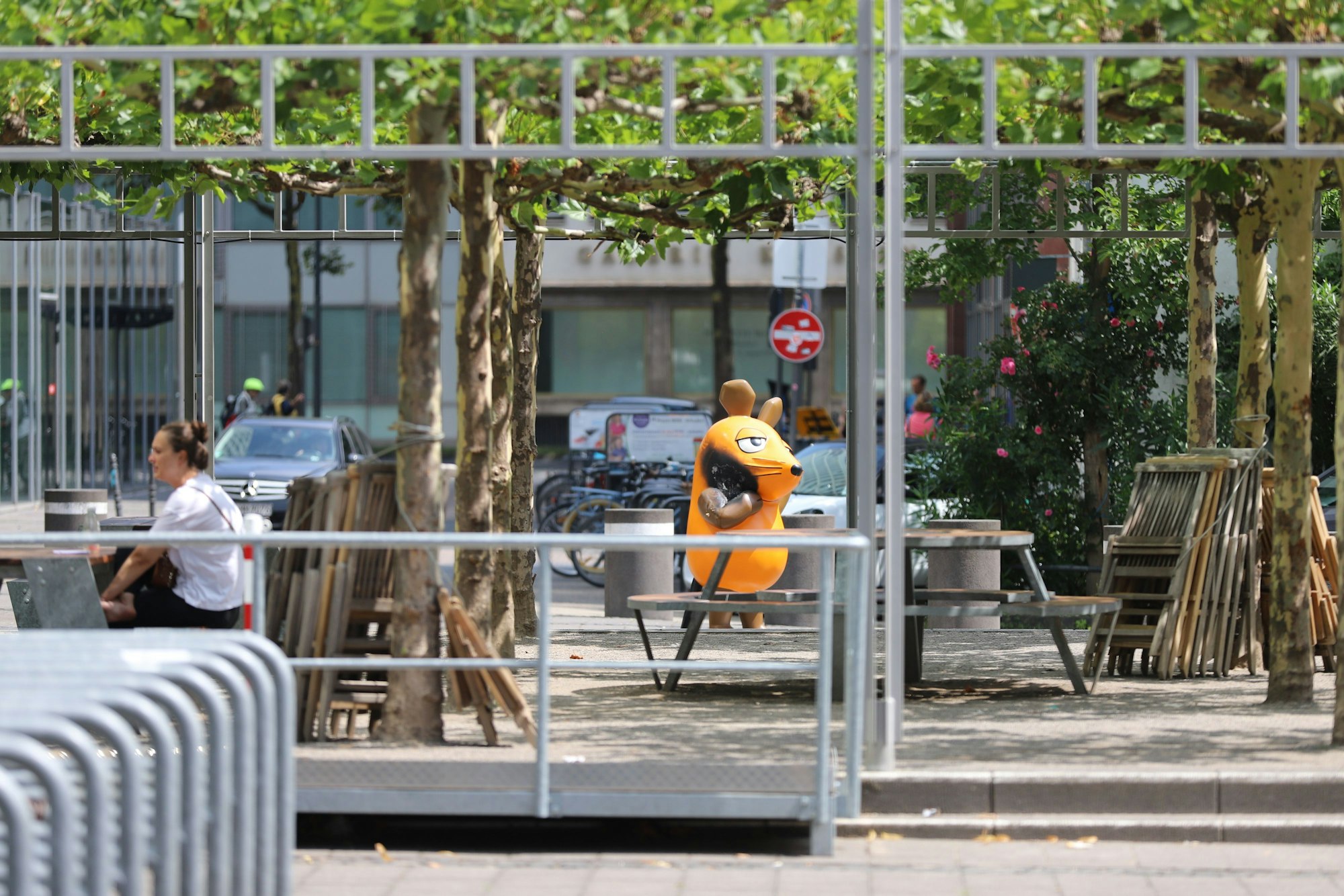 Mit einem großen Brandfleck steht die Maus-Figur hinter einer Sitzfläche vor dem WDR-Gebäude.