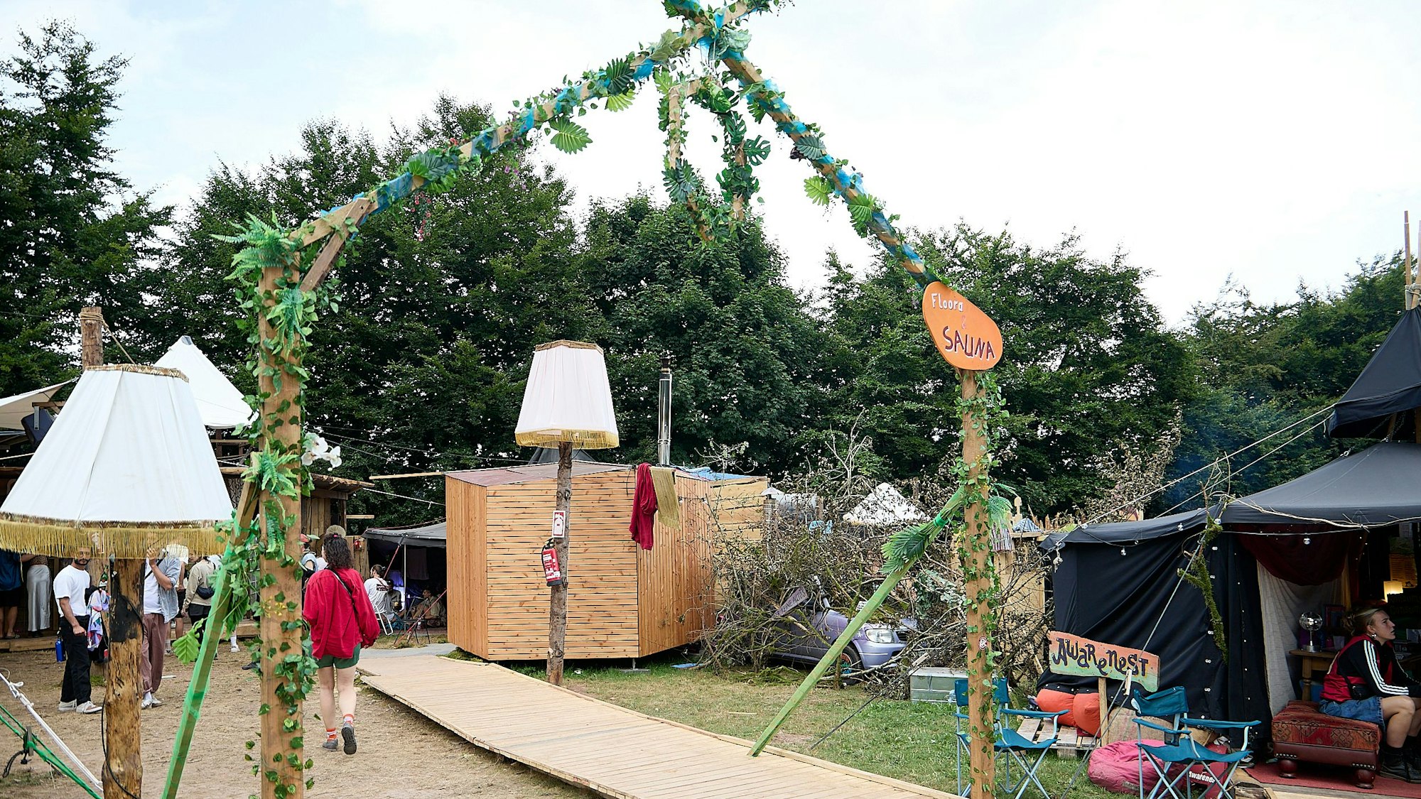 Ein improvisiertes Tor aus Holz und Plastikpflanzen markiert den Eingang zum Saunabereich.