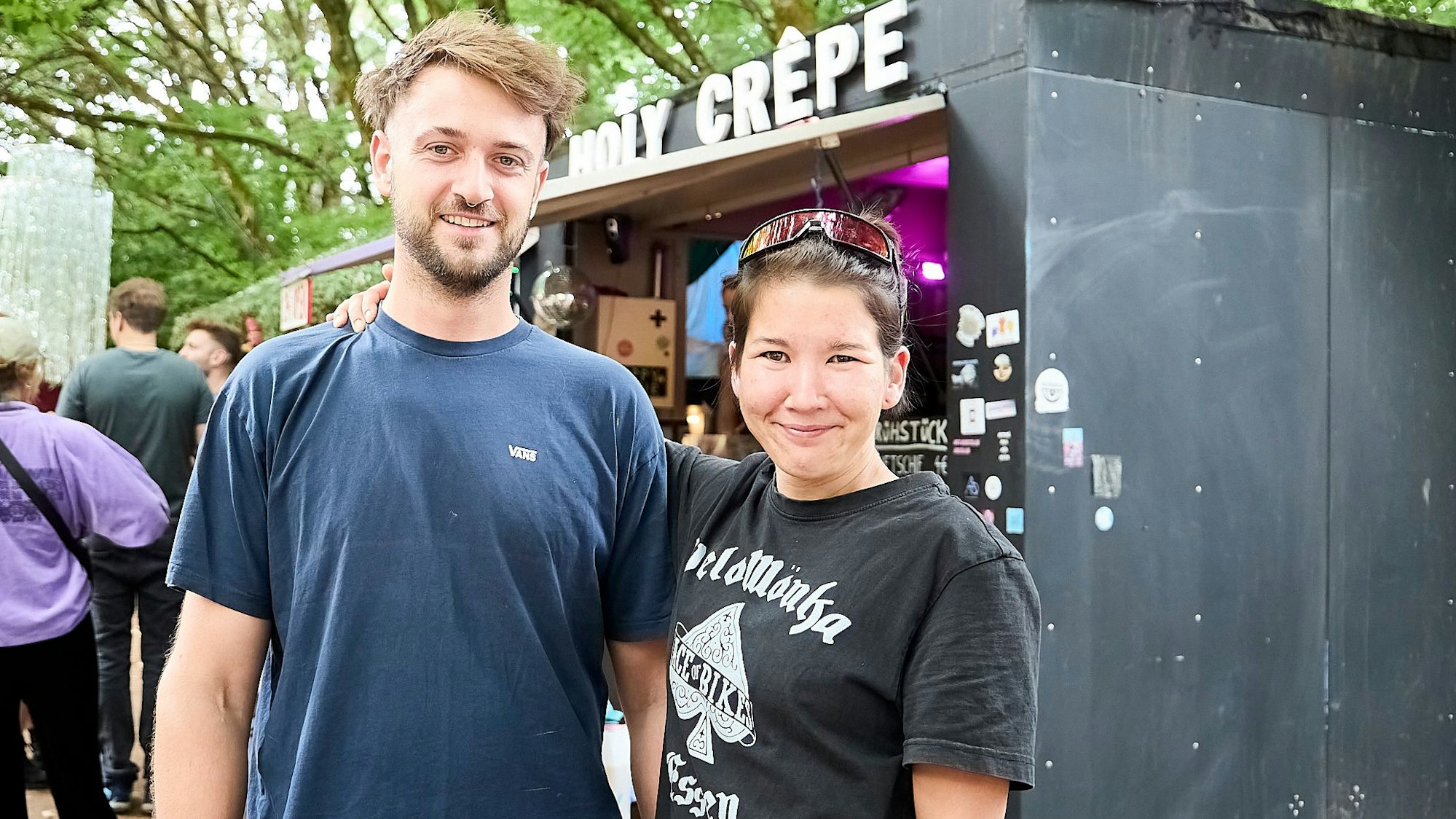 Ein junges Pärchen steht vor seinem Crêpe-Wagen und lächelt in die Kamera.