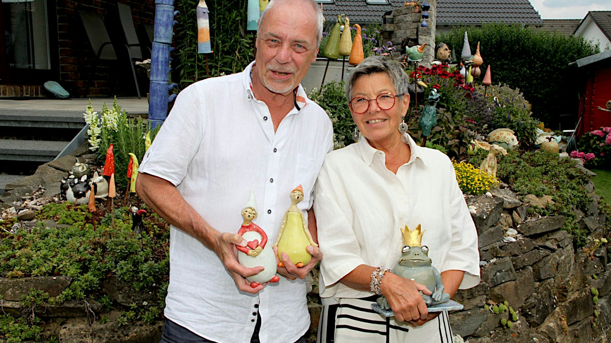 Eine Künstlerin und ihr Ehemann halten Figürchen in ihren Händen, darunter einen Froschkönig aus Keramik.