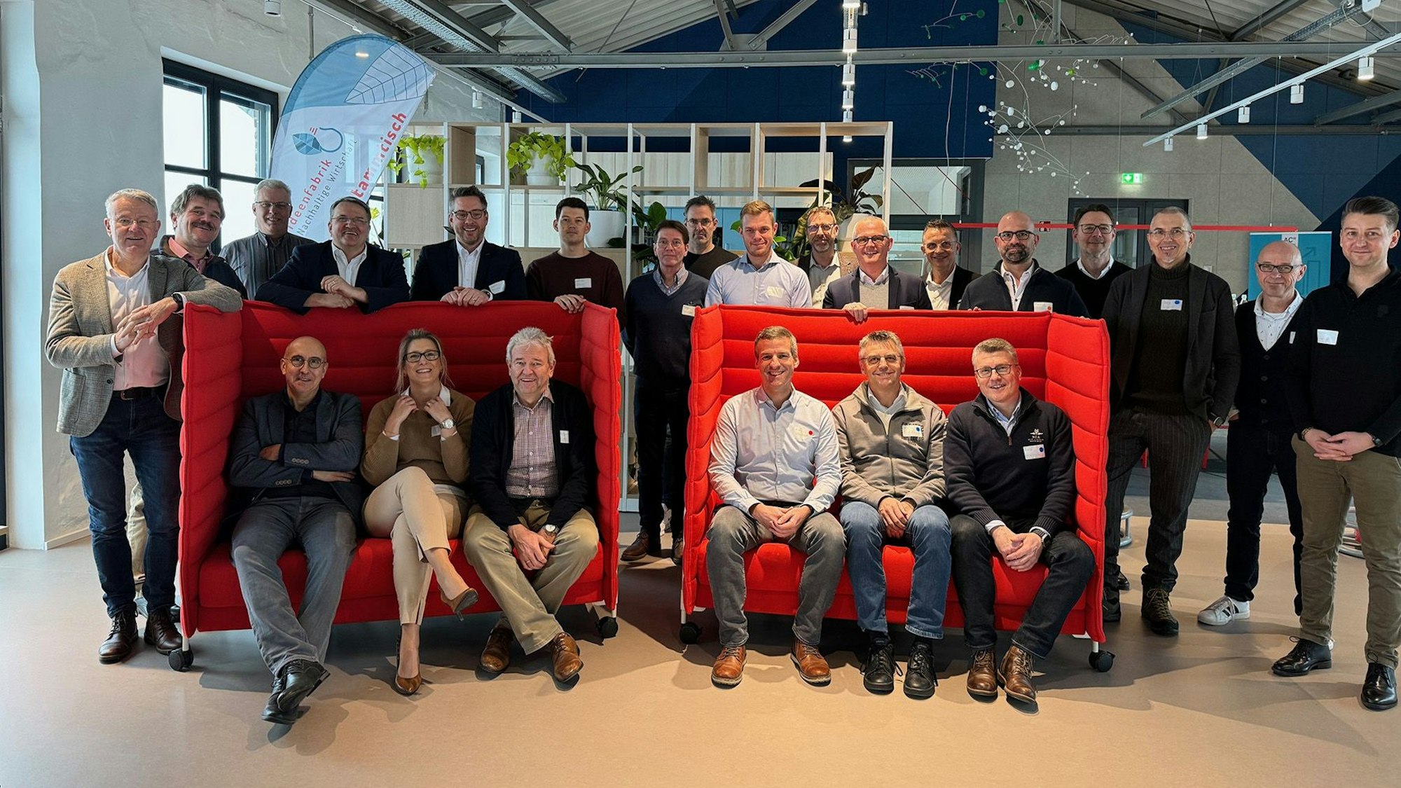 Gruppenfoto des Vorstands und der Führungskräfte der KSK Euskirchen. Sechs Leute sitzen auf zwei roten Sitzbänken, die übrigen haben sich dahinter gruppiert.