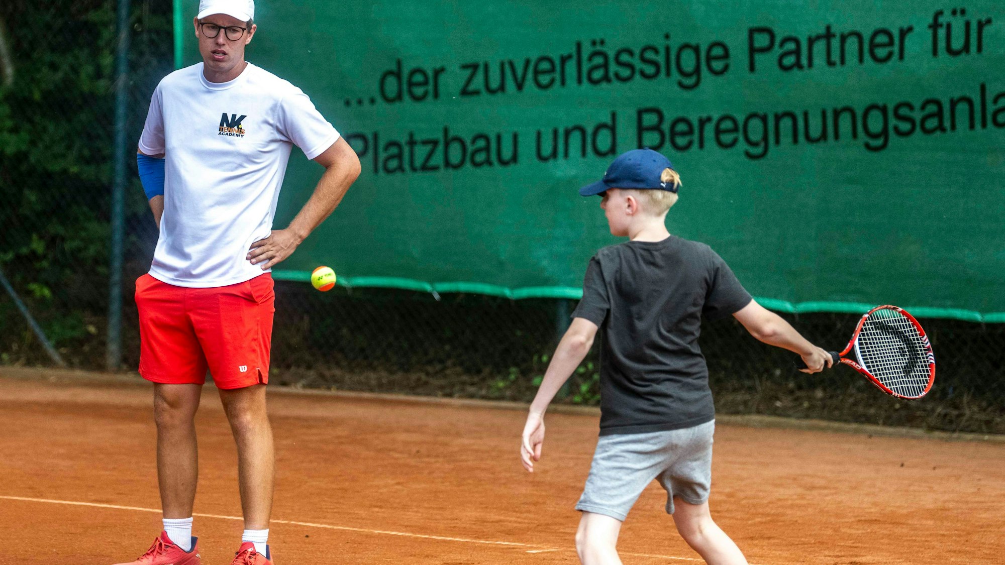 Tennistrainer Niklas Koch schaut einem Kind beim Tennisspielen zu.