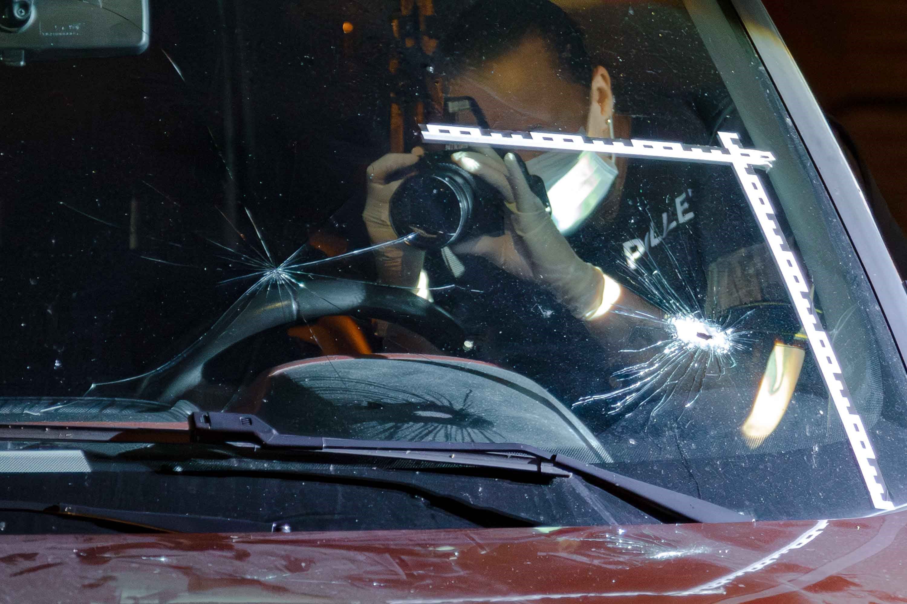Ein Polizeibeamter fotografiert Einschusslöcher in einer Windschutzscheibe.