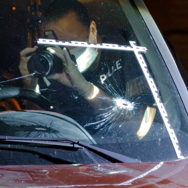 Ein Polizeibeamter fotografiert Einschusslöcher in einer Windschutzscheibe.
