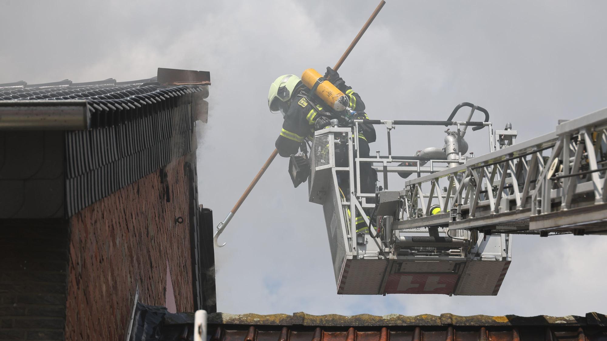 Der Feuerwehrmann, der Atemschutz trägt, stößt den Einreißhaken in die Dachziegel.