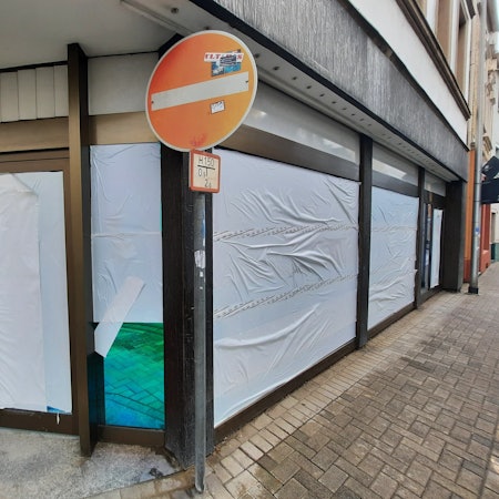 Weiße Folien sind auf die Scheiben eines Ladenlokals geklebt.