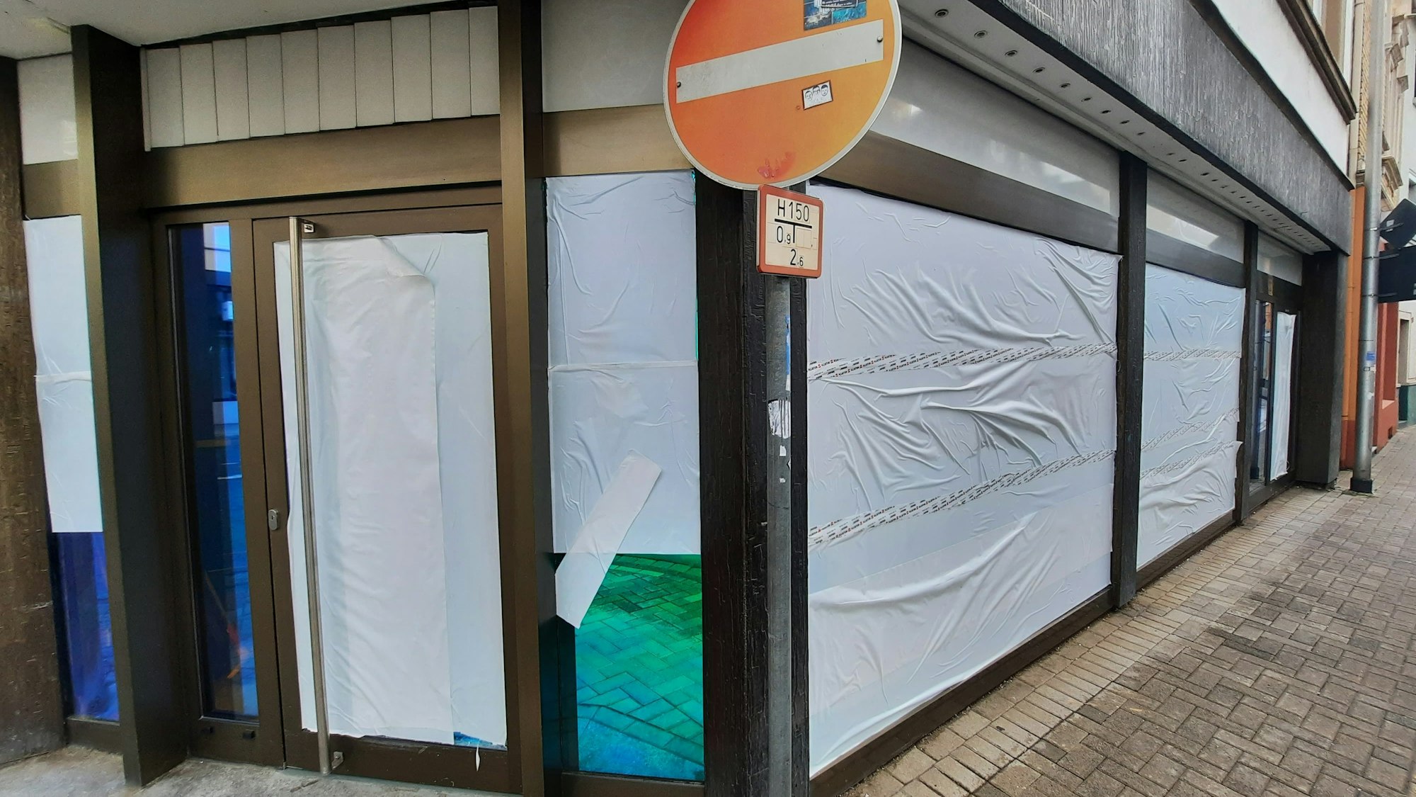 Weiße Folien sind auf die Scheiben eines Ladenlokals geklebt.