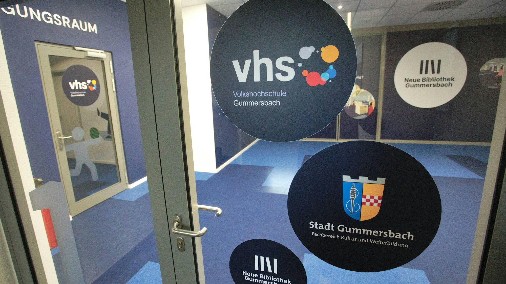 Eine Glastür mit mehreren Aufkleber der Volkshochschule, sowie der Stadt Gummersbach.