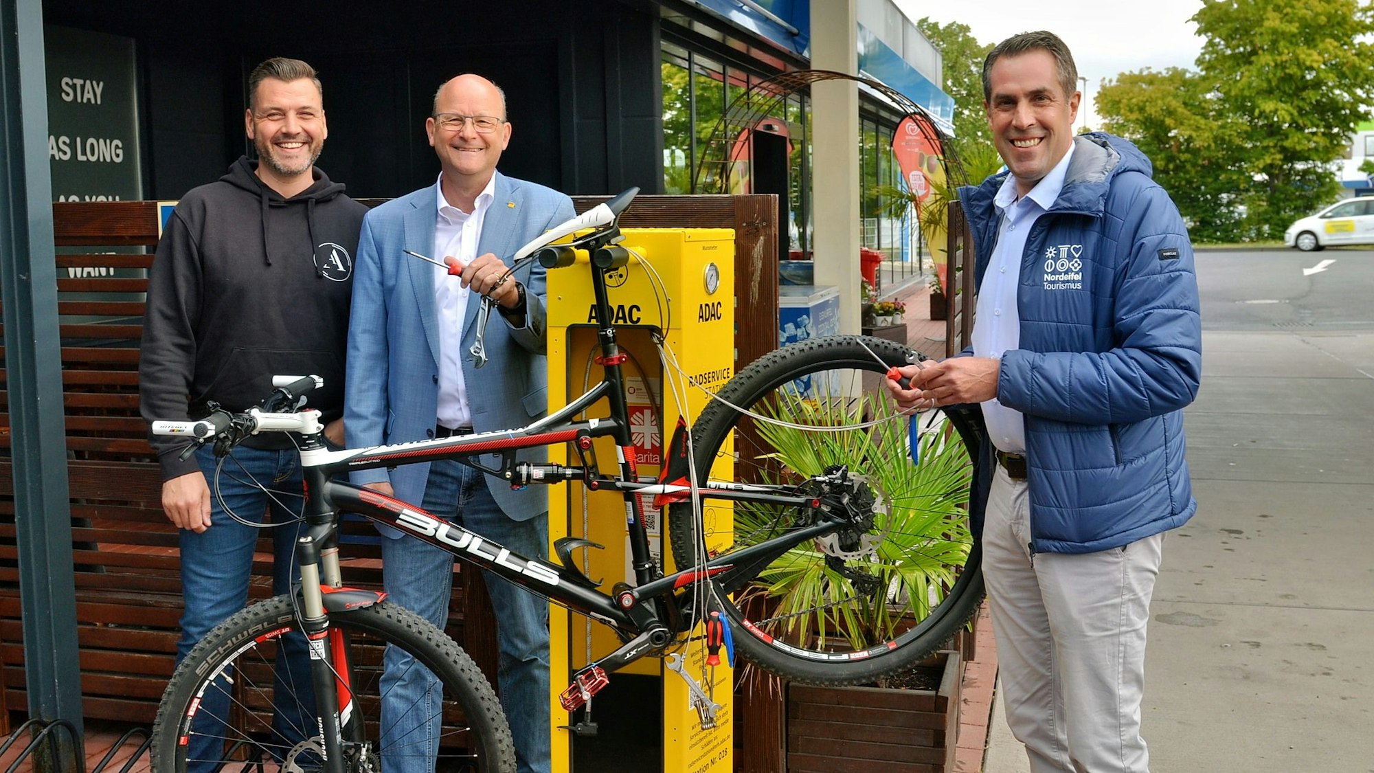 André Schiebahn (v.l.), Thomas Velling und Patrick Schmidder stehen neben der Servicestation, an der ein Fahrrad befestigt ist.
