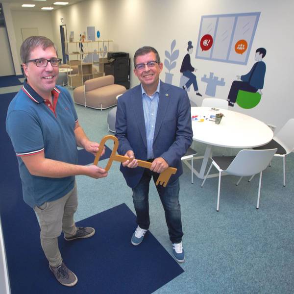 Zwei Männer stehen nebeneinander und halten einen überdimensionalen Holzschlüssel in der Hand.