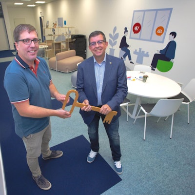 Zwei Männer stehen nebeneinander und halten einen überdimensionalen Holzschlüssel in der Hand.