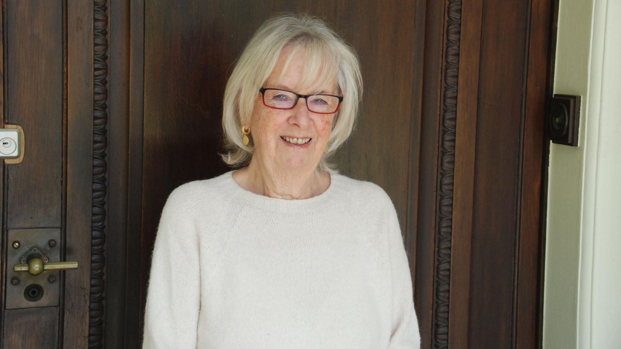 Vera von Schnitzler trägt eine Brille und lächelt vor einer verschlossenen Tür.
