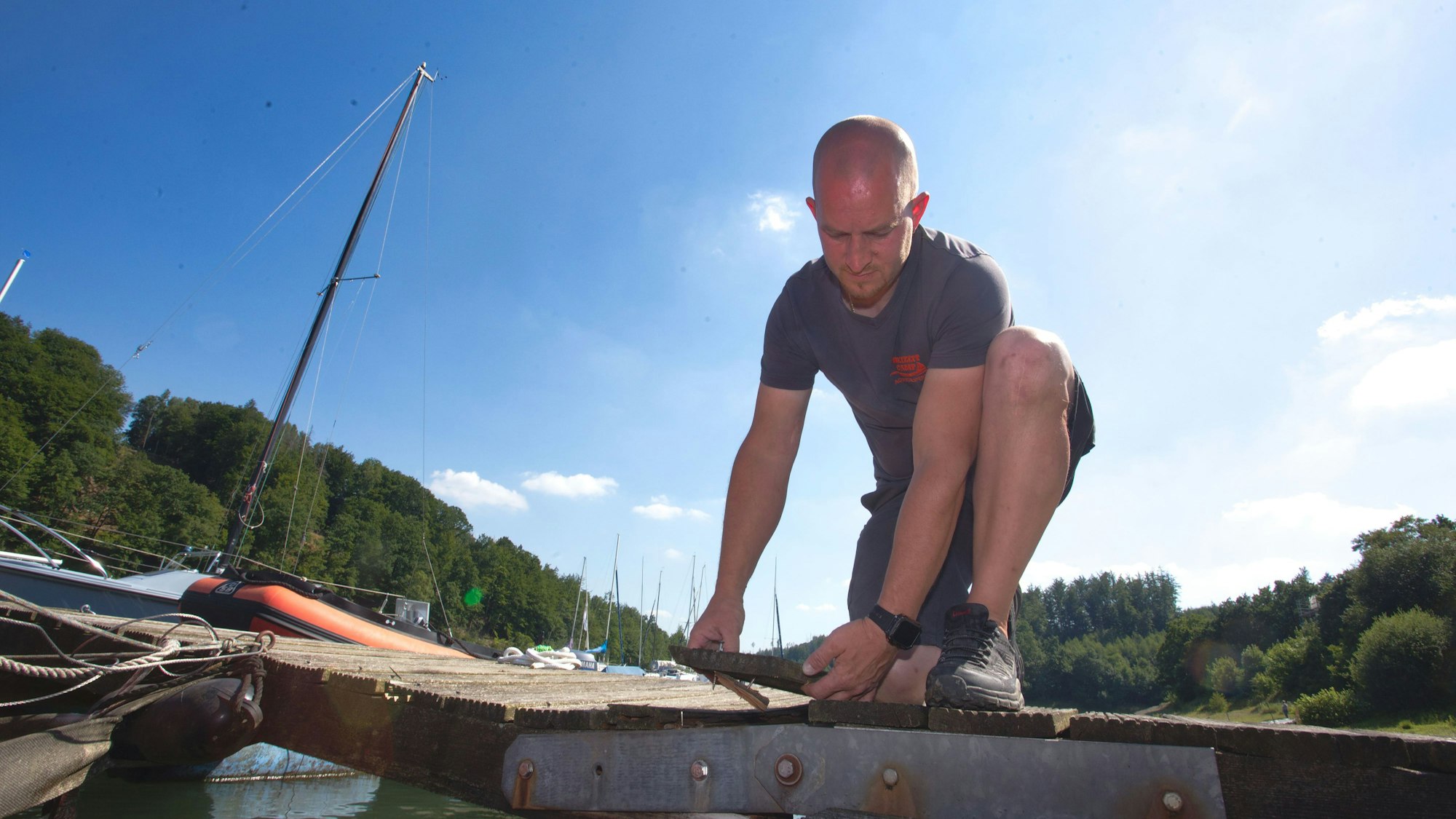 Ein Mann Arbeitet an einem Steg. Neben ihm stehen ein paar Boote.