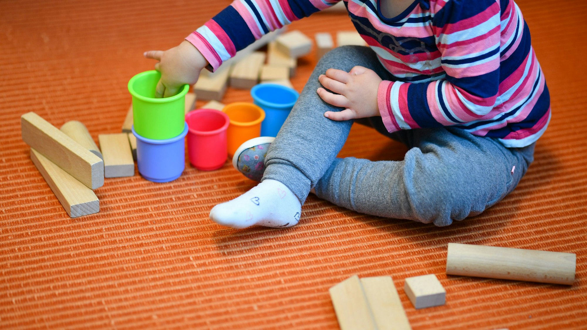 Ein Mädchen spielt in einer Kita mit bunten Bechern und Bauklötzen. (Archivbild)