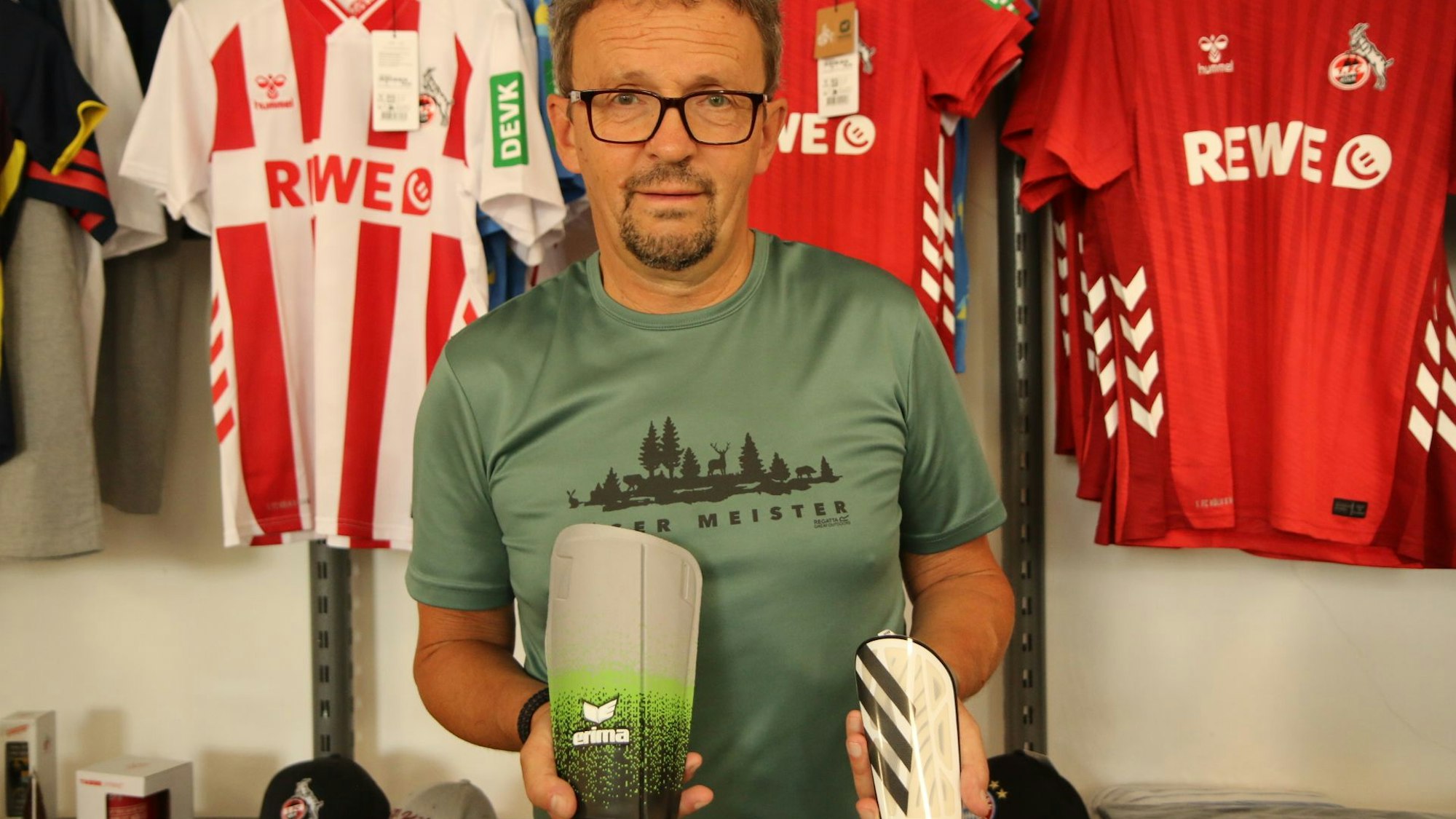 Sportgeschäft-Inhaber Wolfgang Fröhling hält einen kleinen und einen großen Schienbeinschoner in den Händen.