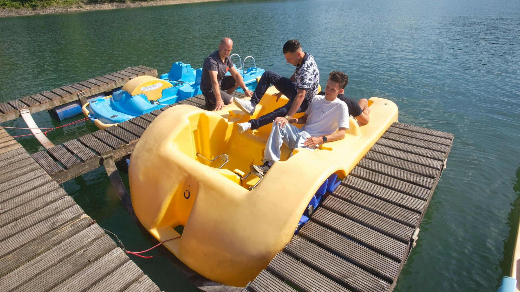 Drei Jungs in einem gelben Tretboot bekommen am Steg vom Besitzer die Regeln erklärt.