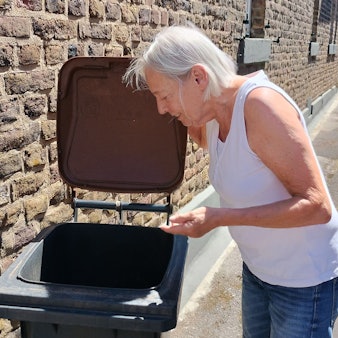 Das Bild zeigt, wie die Seniorin ihre Tonne öffnet und hineinschaut.