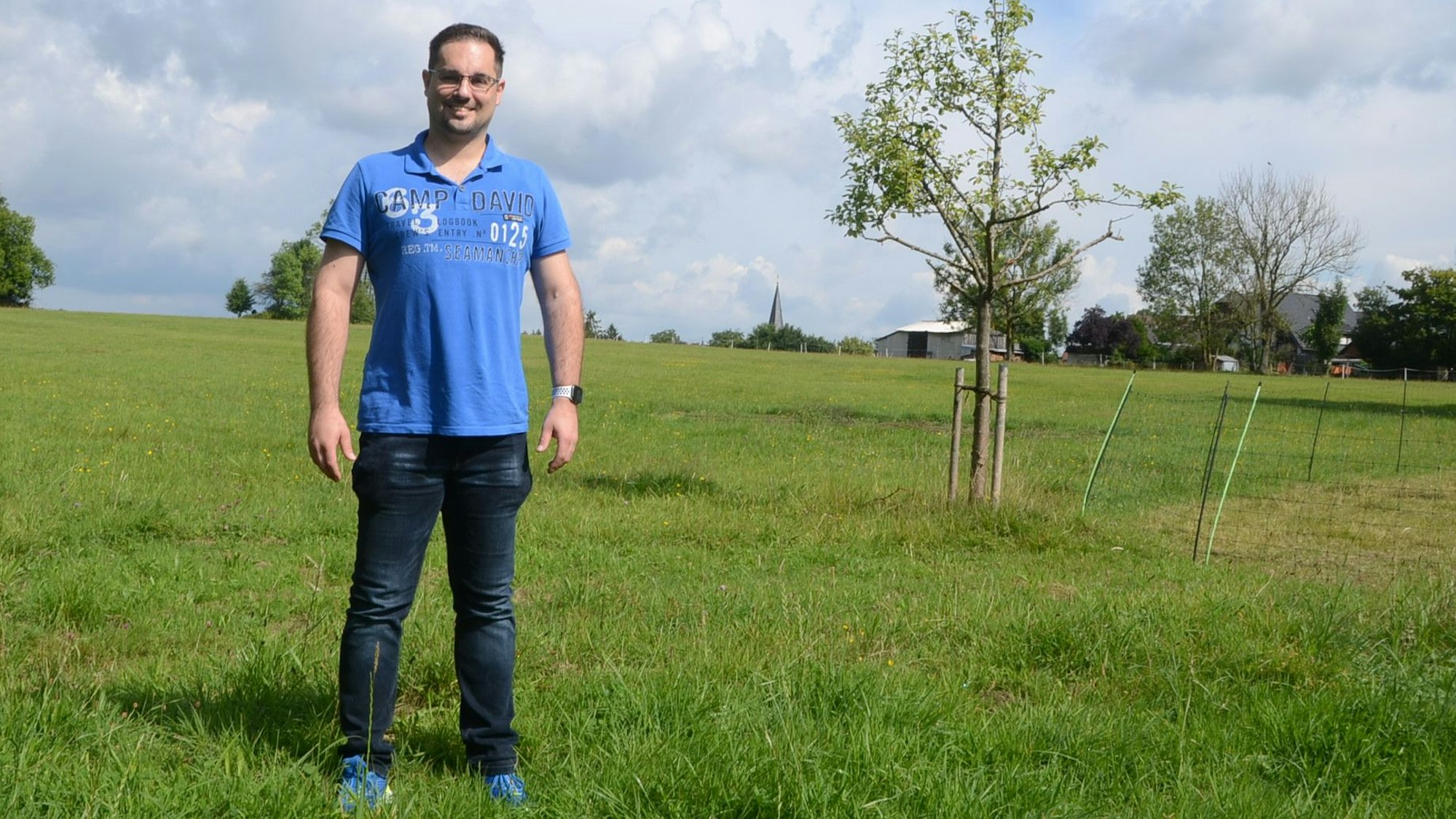 Ein Mann im blauen Polohemd steht auf einer Wiese.