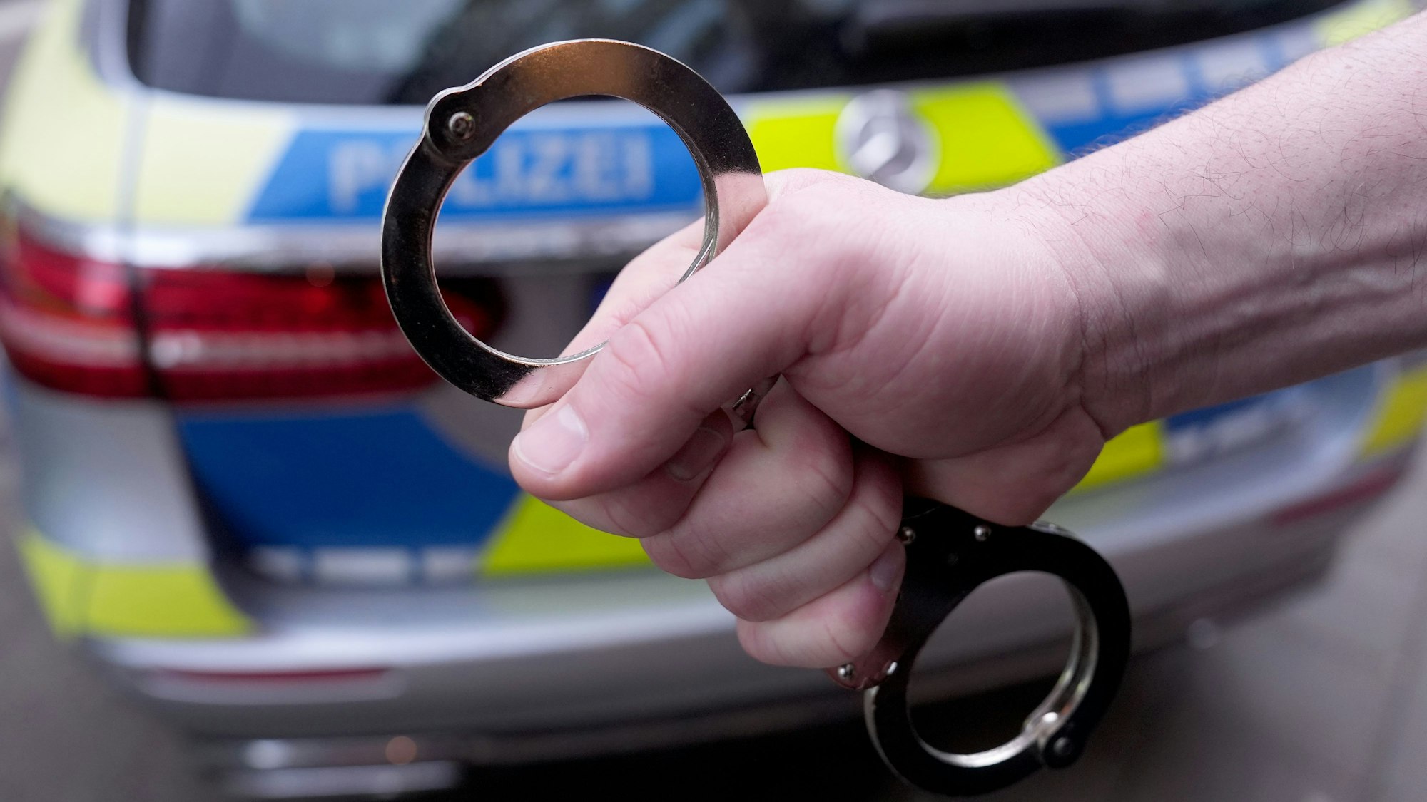 Ein Polizist hält Handschellen vor einem Einsatzfahrzeug hoch.