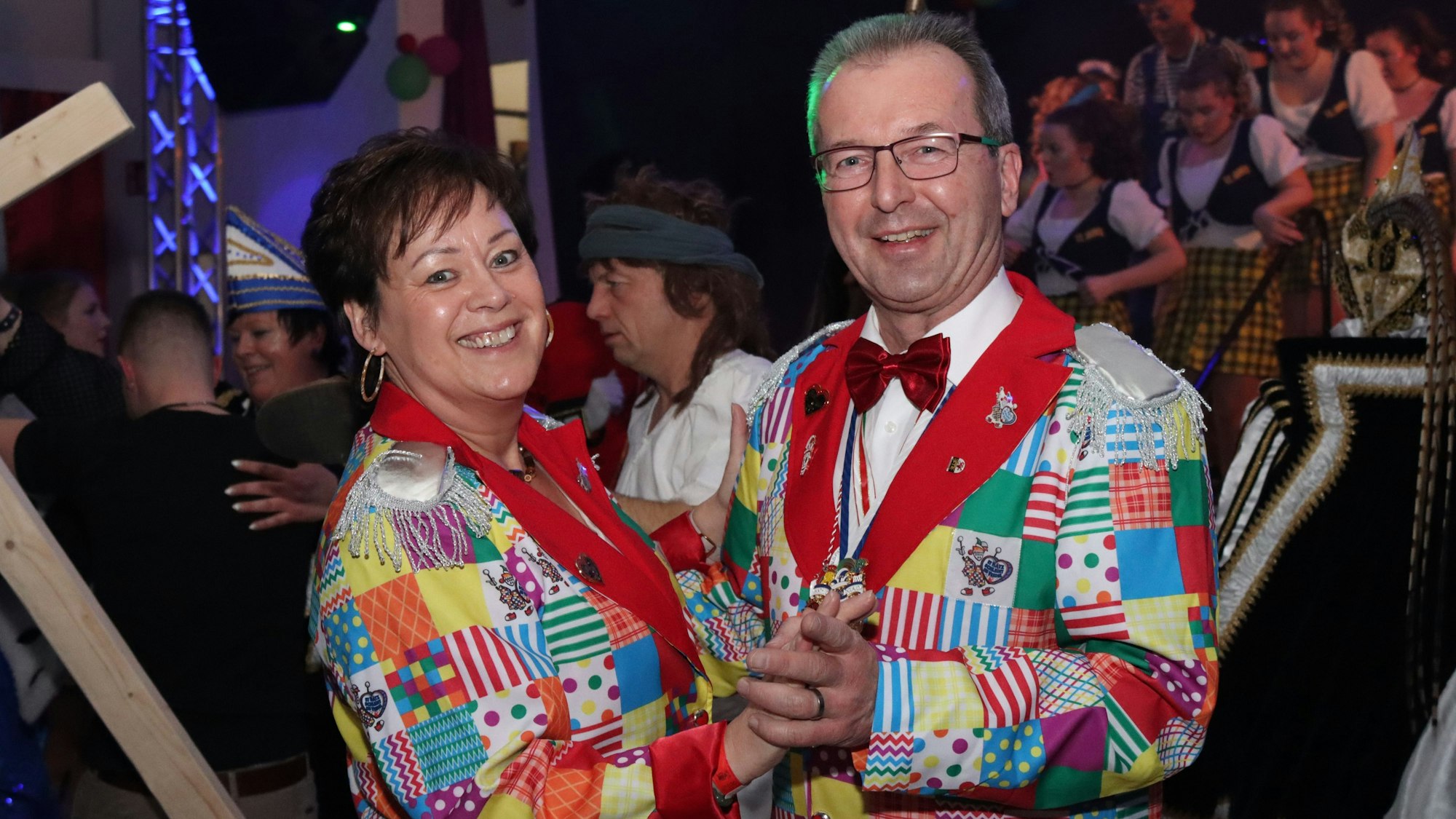 Eine Frau und ein Mann tanzen zusammen und tragen einen kunterbunten Karnevalsanzug.