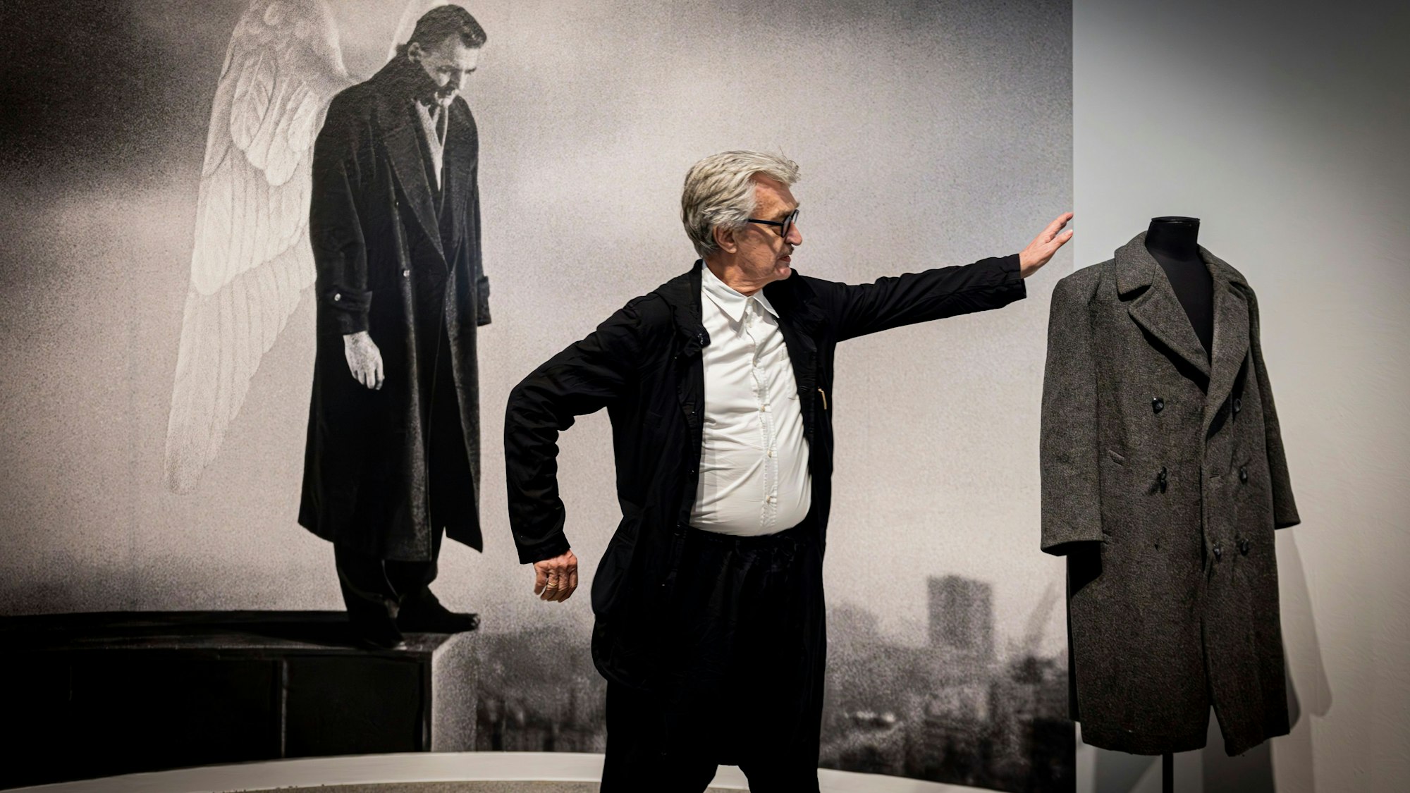 Wim Wenders in der Ausstellung vor Bild und requisite von "Der Himmel über Berlin"