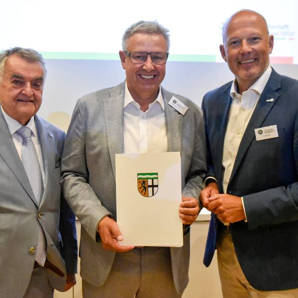 Das Bild zeigt drei Männer, einer hält eine Urkunde in seinen Händen.