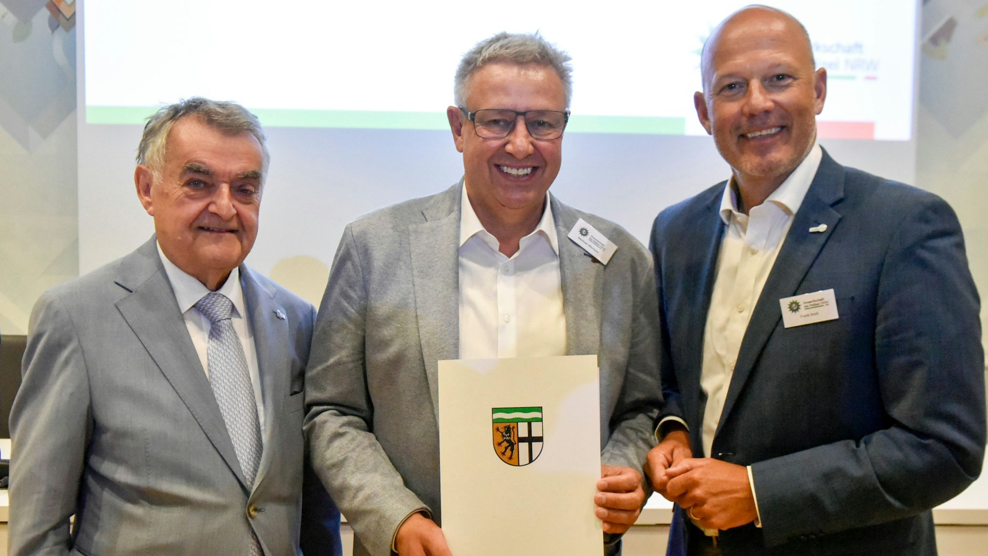 Das Bild zeigt drei Männer, einer hält eine Urkunde in seinen Händen.