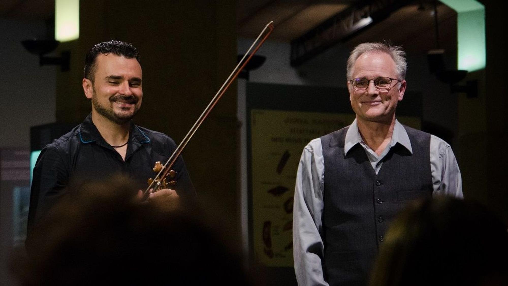 Zwei Herren, der rechte hält eine Violine in der Hand.