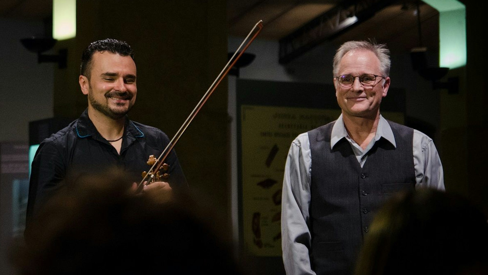 Zwei Herren, der rechte hält eine Violine in der Hand.