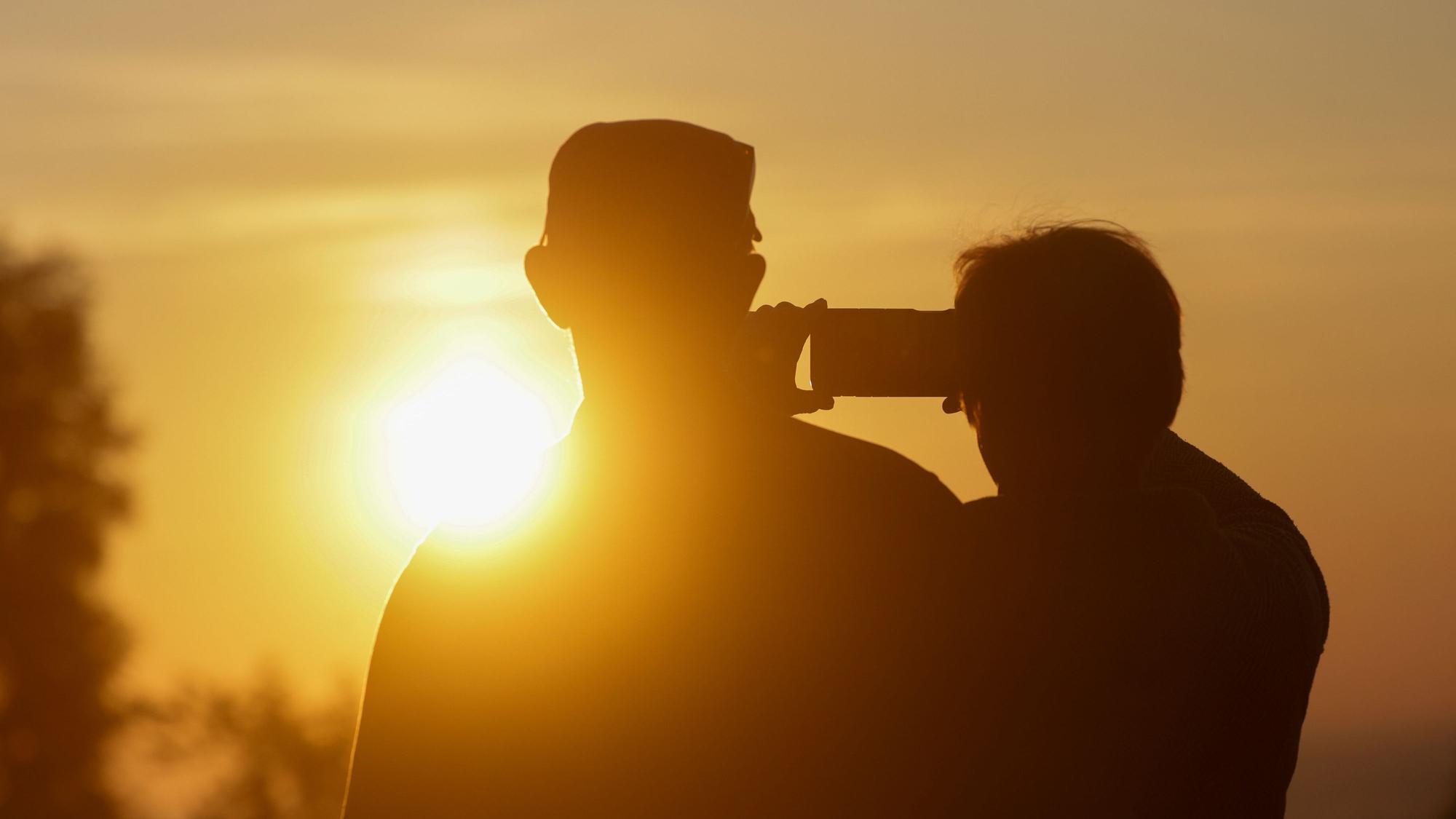 Ein Mann und eine Frau fotografieren mit einem Handy den Sonnenaufgang.