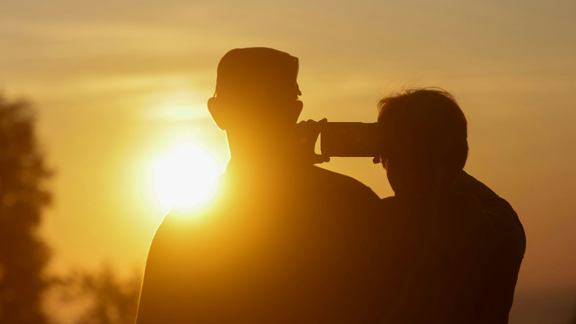 Ein Mann und eine Frau fotografieren mit einem Handy den Sonnenaufgang.