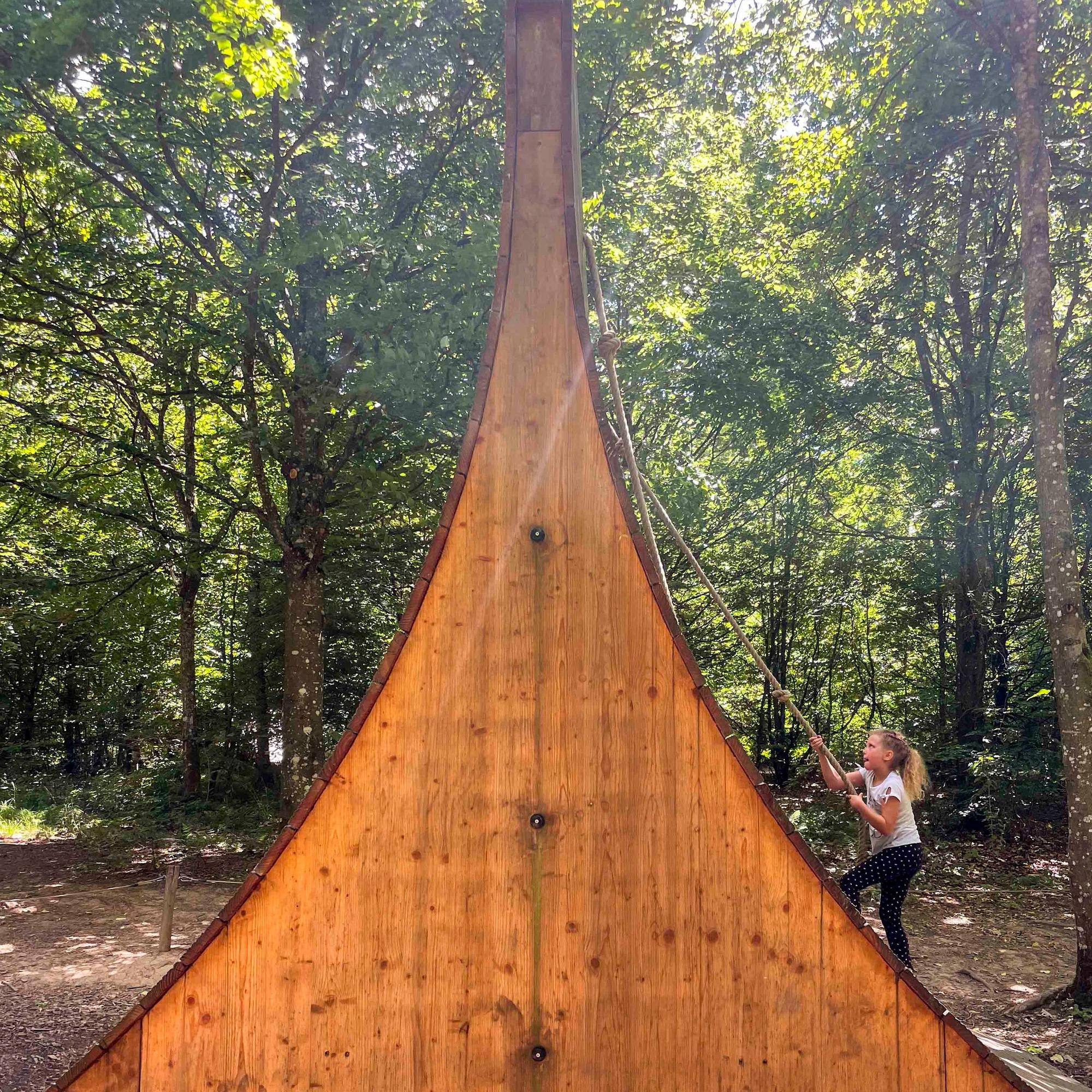 Ein Mädchen klettert mithilfe eines Seils eine aus Holz gebaute Steilwand hinauf.