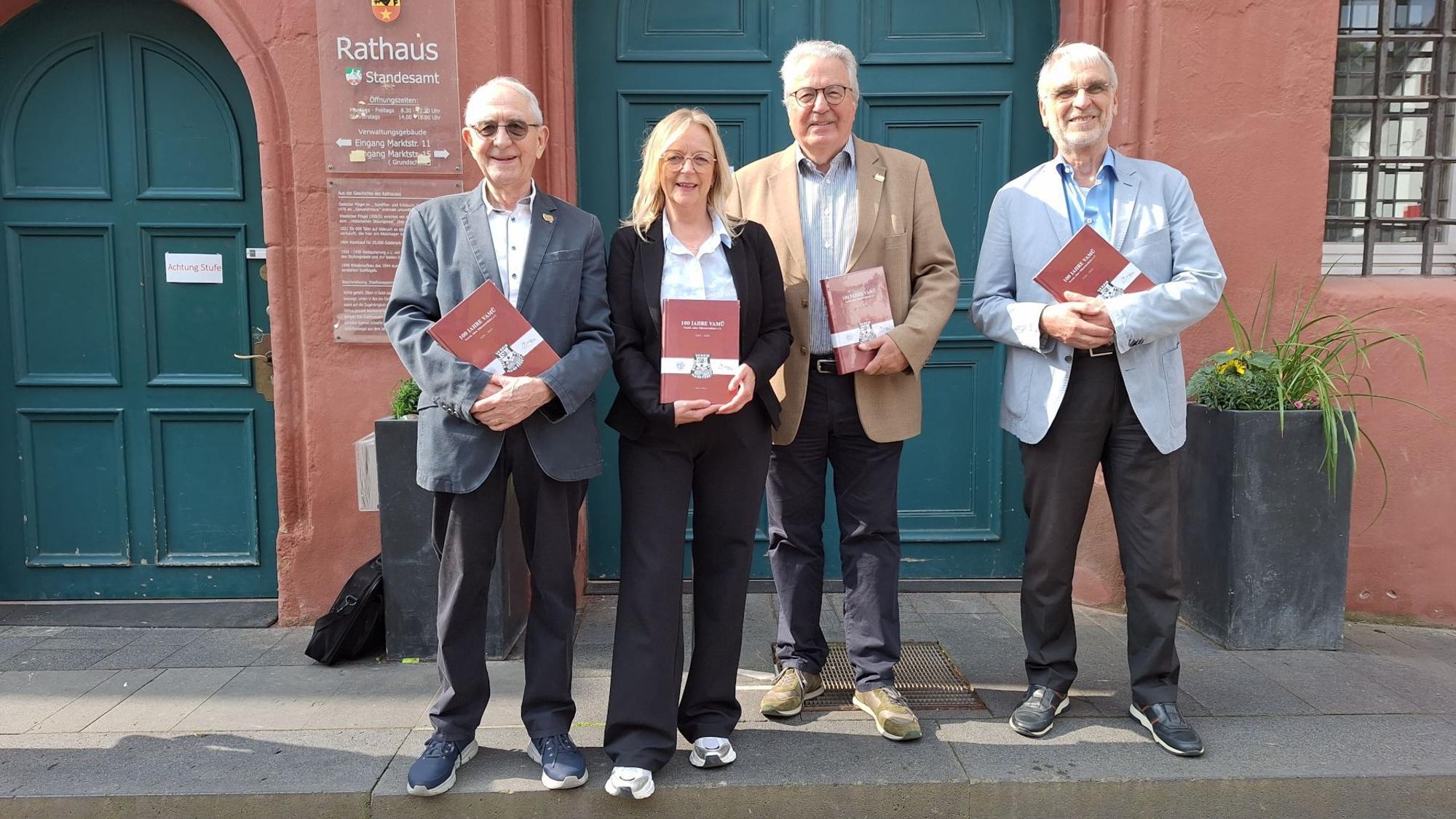 Drei Männer und eine Frau stehen vor dem Rathaus in Bad Münstereifel. Jeder von ihnen hält ein rotes Buch in den Händen.