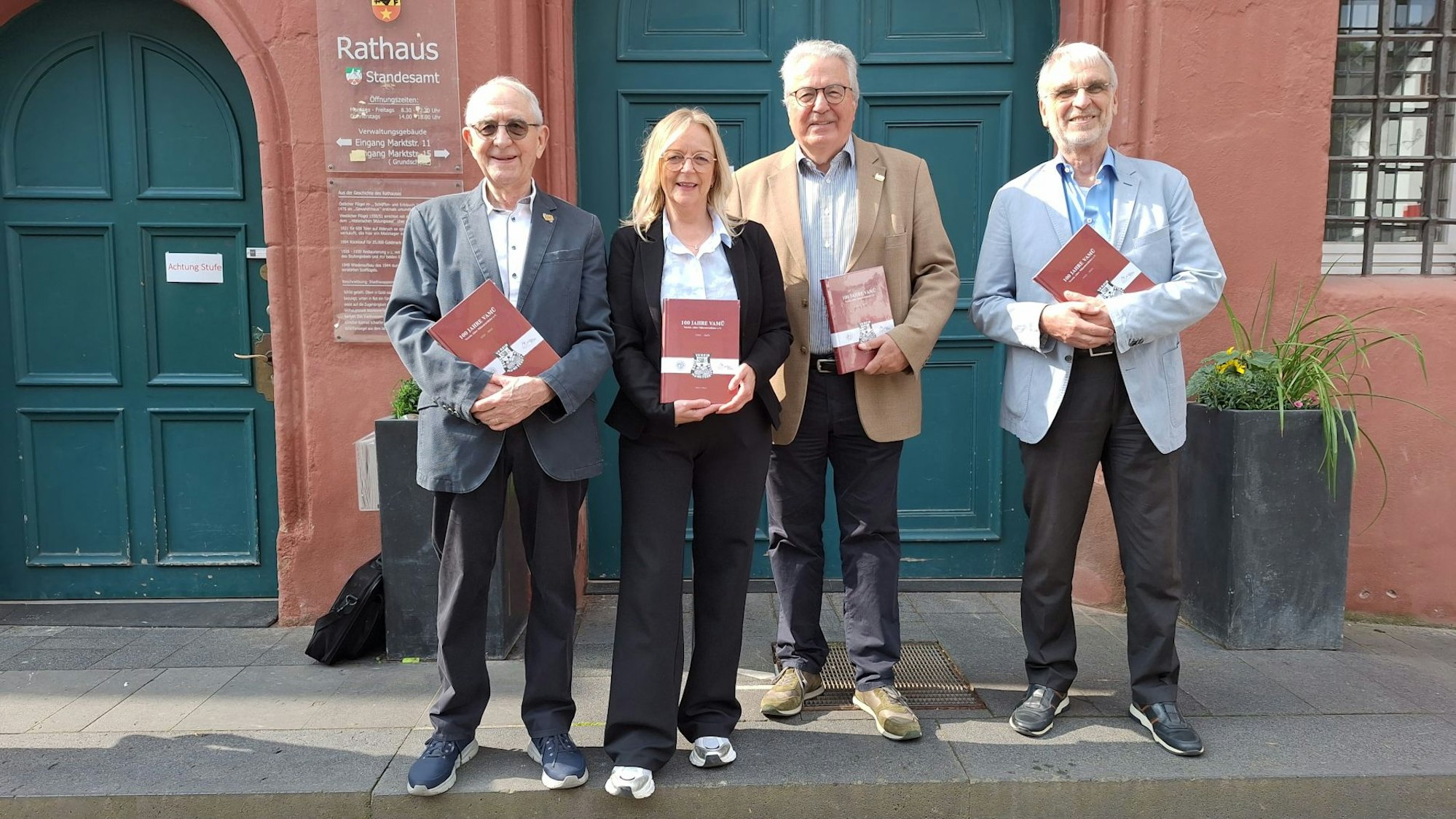 Drei Männer und eine Frau stehen vor dem Rathaus in Bad Münstereifel. Jeder von ihnen hält ein rotes Buch in den Händen.