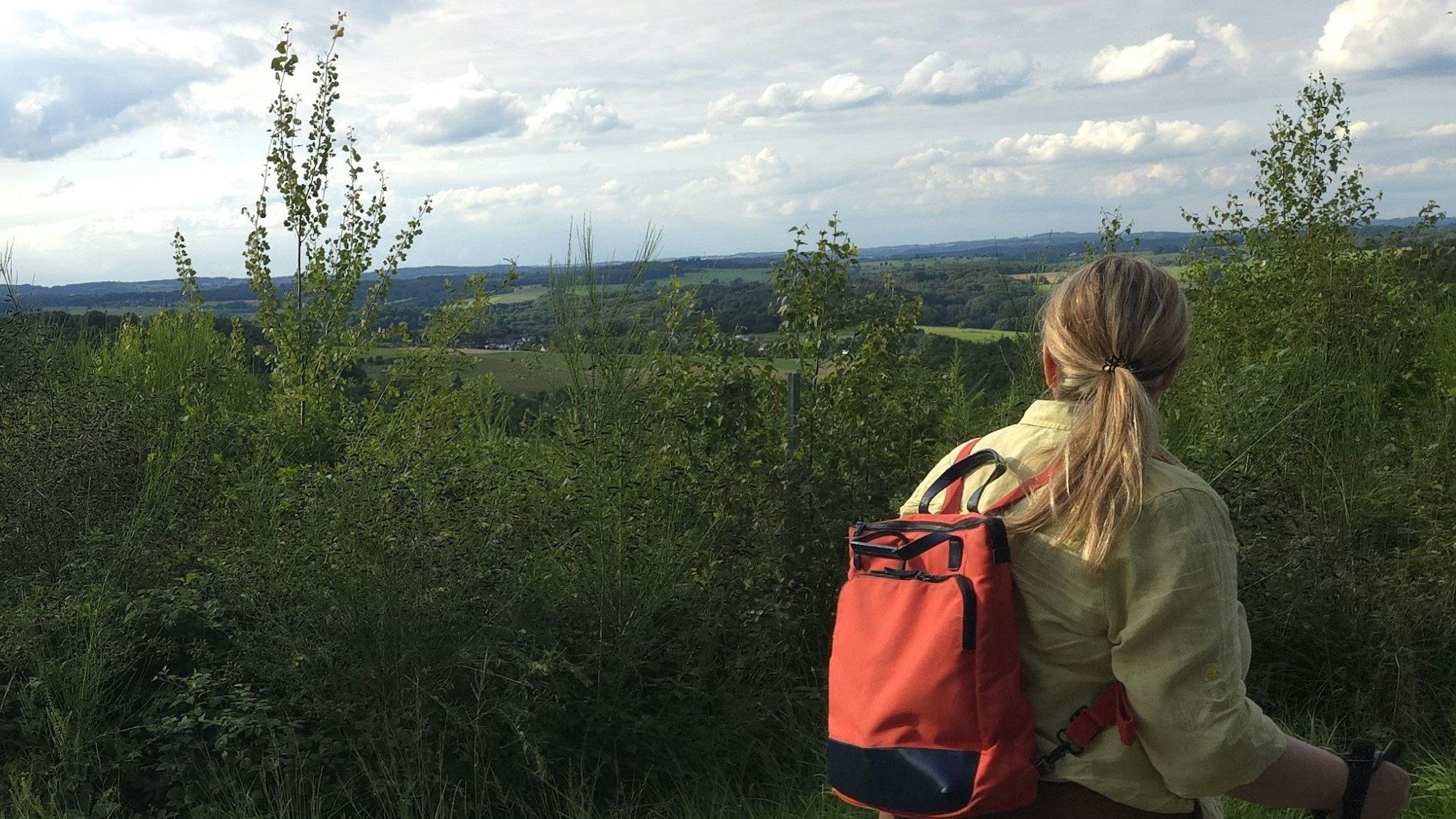 Eine junge Frau genießt bei einer Wanderung den Ausblick auf eine Landschaft.