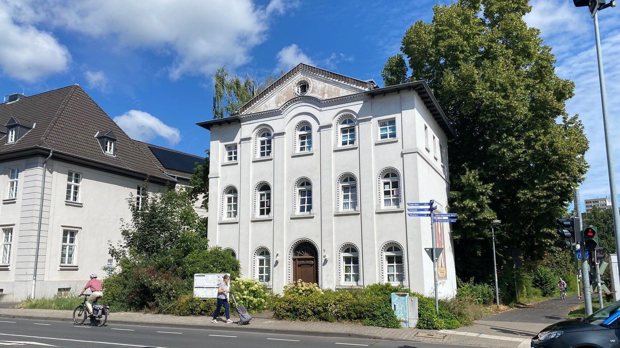Zu sehen ist ein weißes Haus an einer Straße.