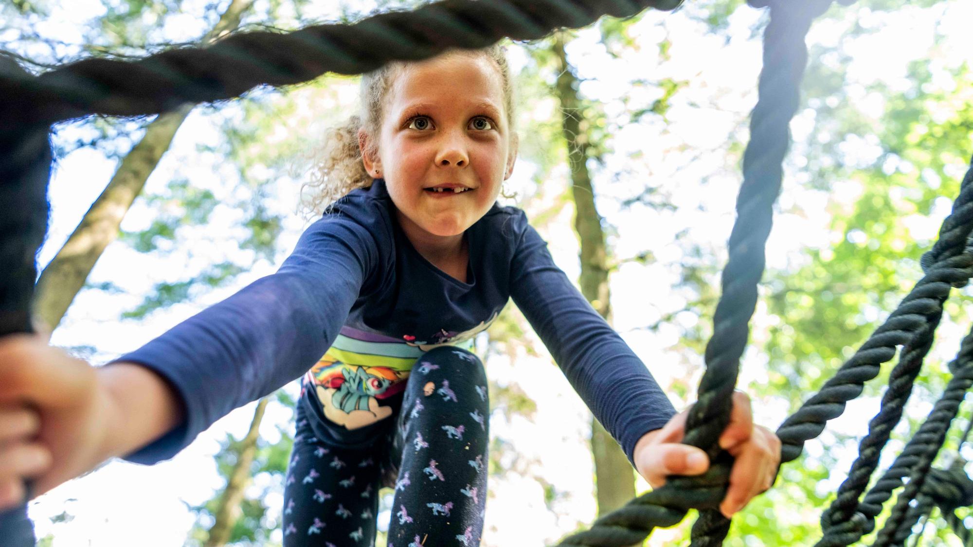 Ein Mädchen klettert in einer Seilwand.
